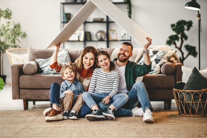 Een gezin met twee kinderen zit glimlachend onder een kartonnen dak