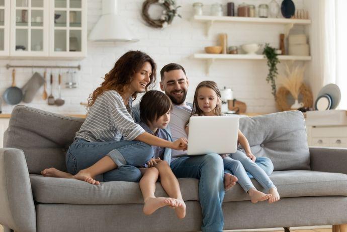 Een gezin zit gezellig thuis in de zetel en kijkt samen naar een laptopscherm